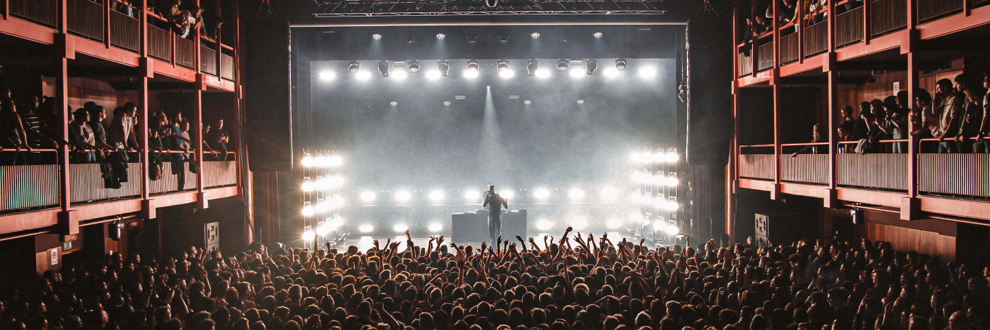 An artist performs in the Main hall on an illuminated stage for large audience.